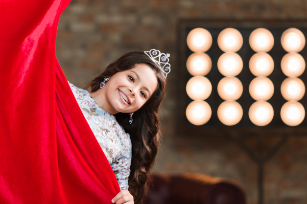 smiling girl with crown her head peeking from red curtain small